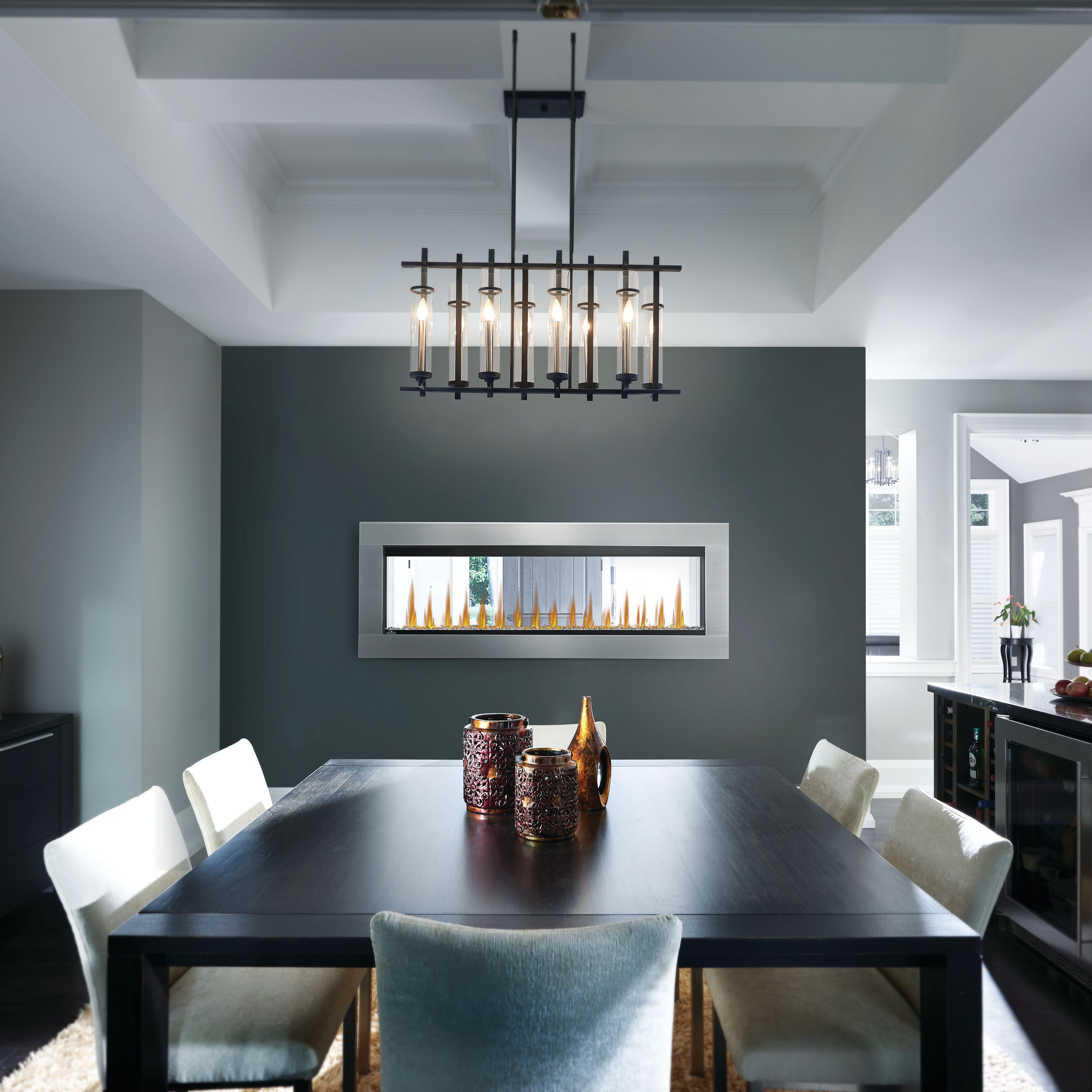 Modern dining room with a black table and chairs, featuring a chandelier and wall-mounted fireplace.