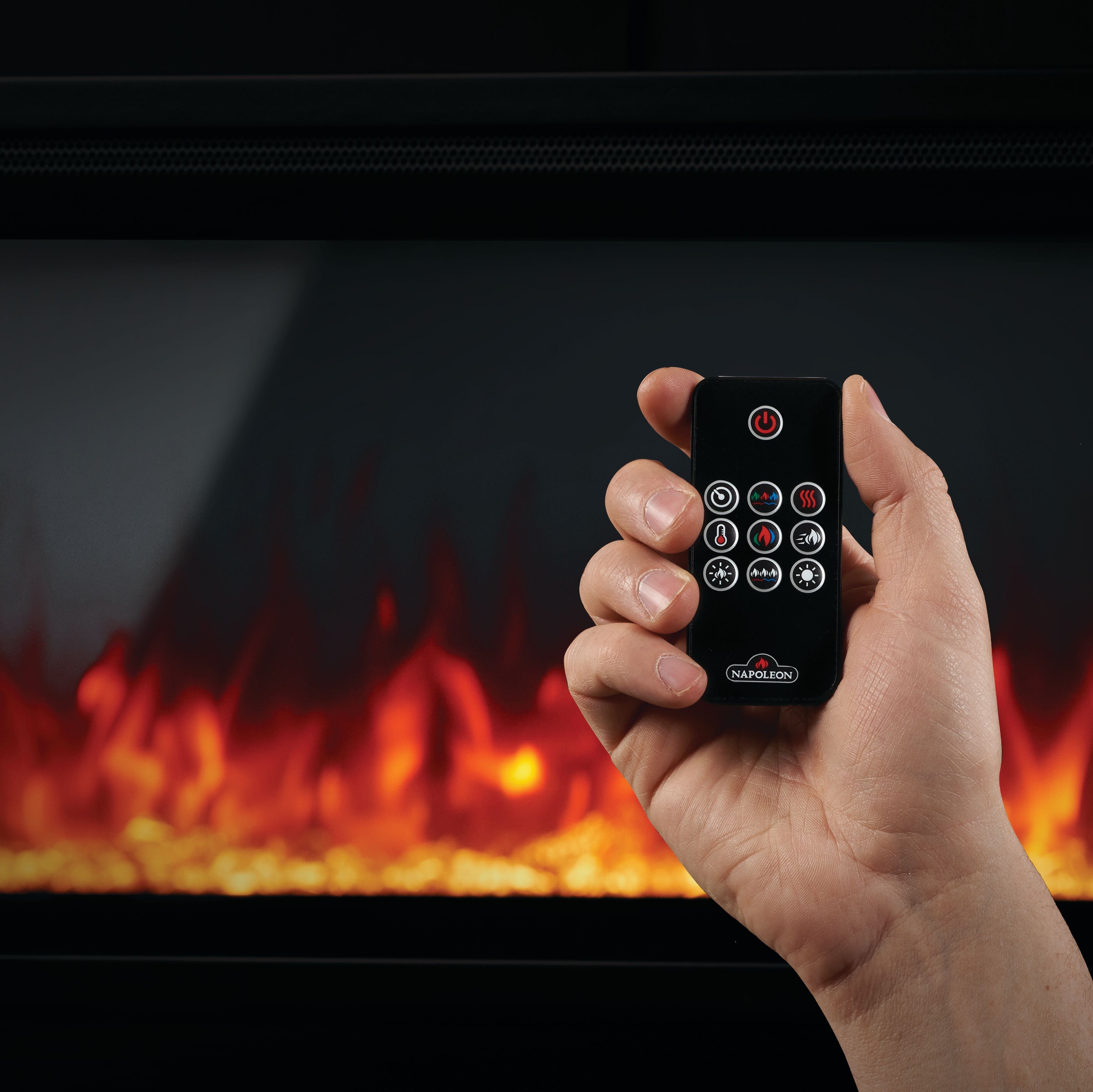 Hand holding a remote control in front of an electric fireplace with flames.